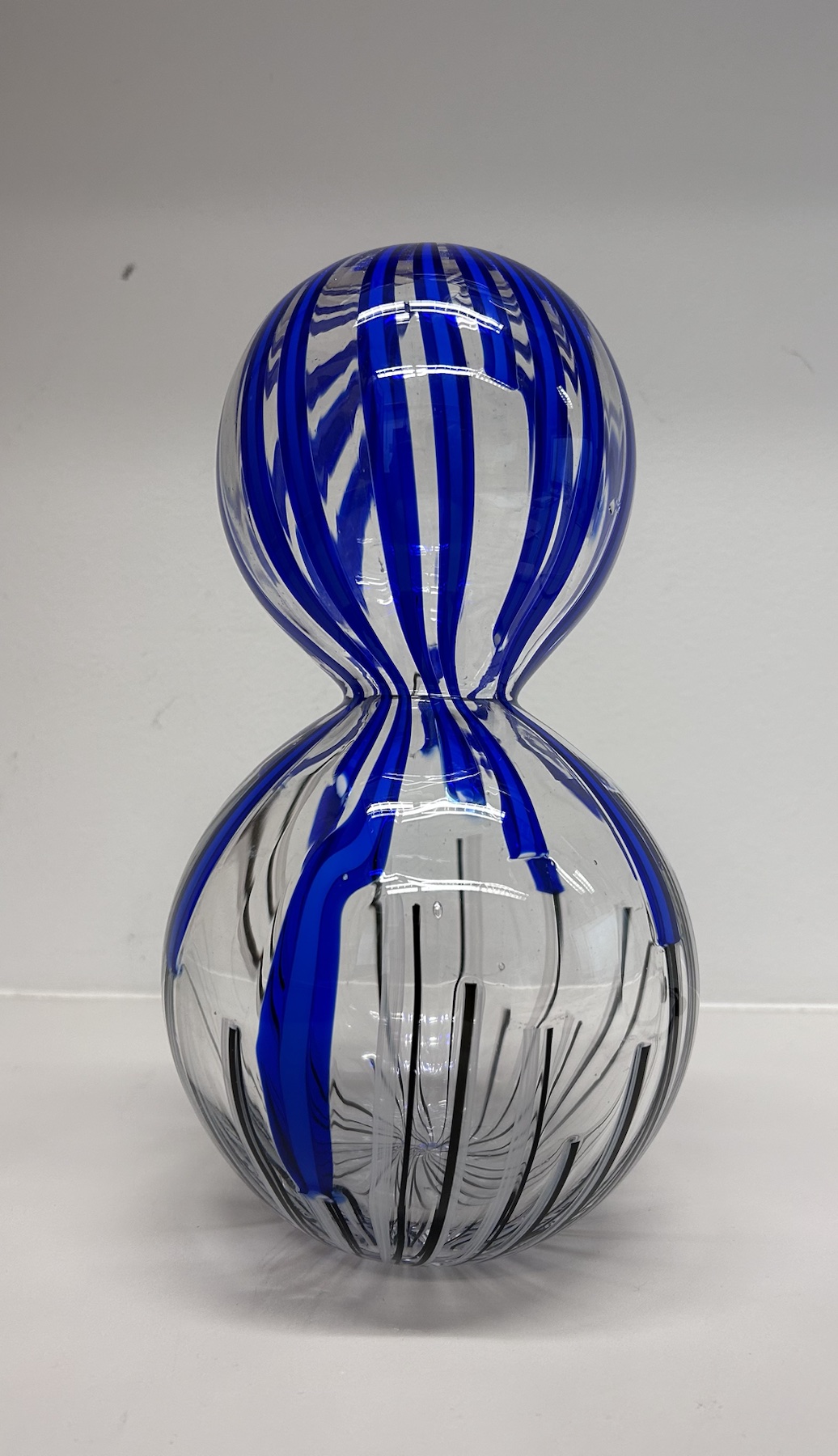 Clear hourglass-shaped glass form with vivid blue and black line work